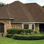 A house with a brick wall and bushes in front of it.