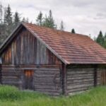Wooden cabin surrounded by trees and grass.