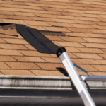 Damaged roof shingles with ladder nearby.