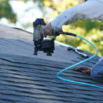 Person using nail gun on roof shingles.