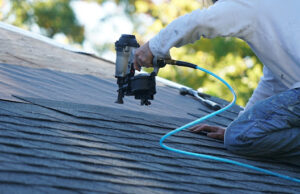 Person using nail gun on roof shingles.