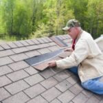 Man repairing roof shingles on house.