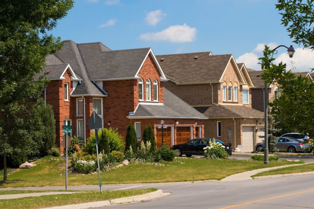 Suburban street with modern brick houses and well-kept lawns under a blue sky.