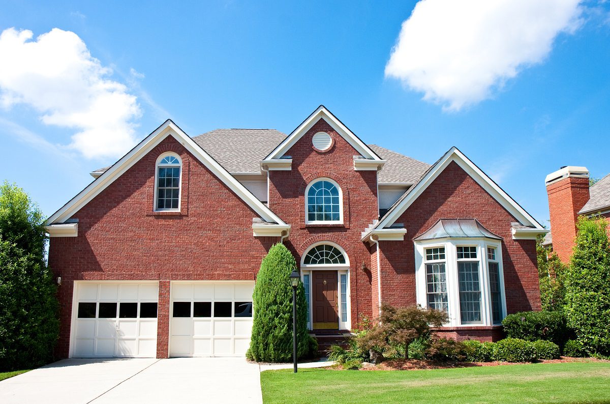 A large brick house with a three-car garage and manicured lawn.