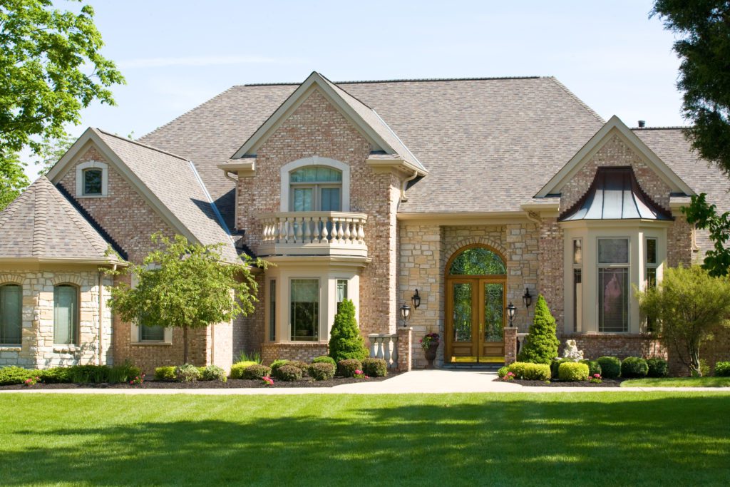 Elegant stone house with lush green lawn and large windows.