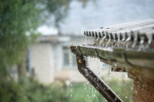 Close-up of a rain gutter draining water from a roof during rainfall.