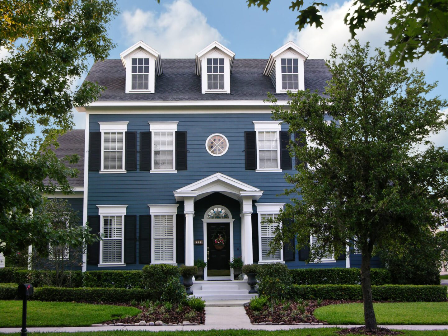 Elegant blue colonial-style house with white trim and lush greenery.