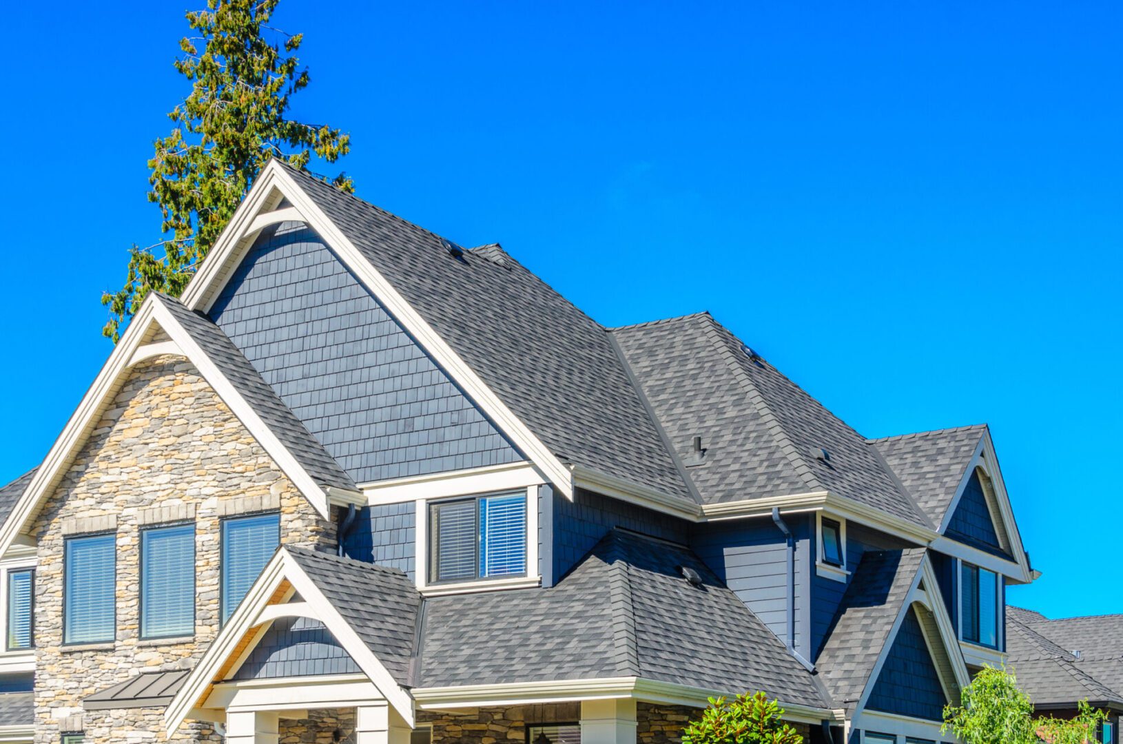 A modern house with gray shingles and stone accents under a clear blue sky.