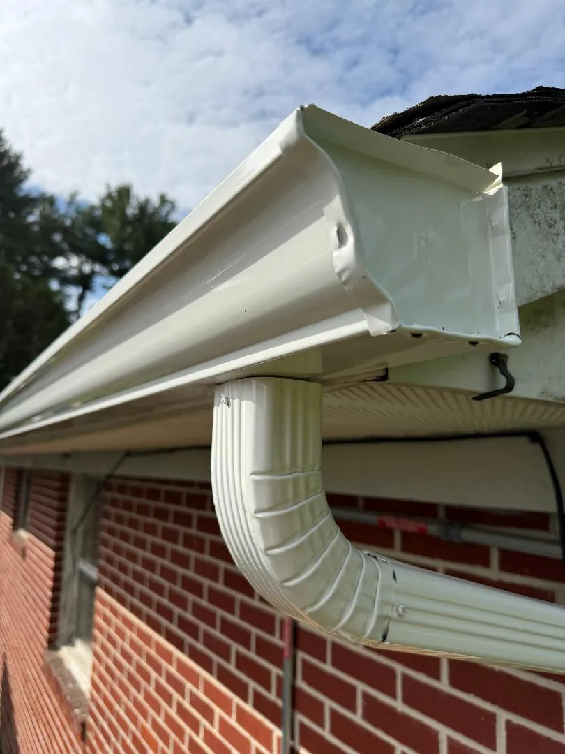 White aluminum rain gutter with end cap and downspout elbow on a brick house.