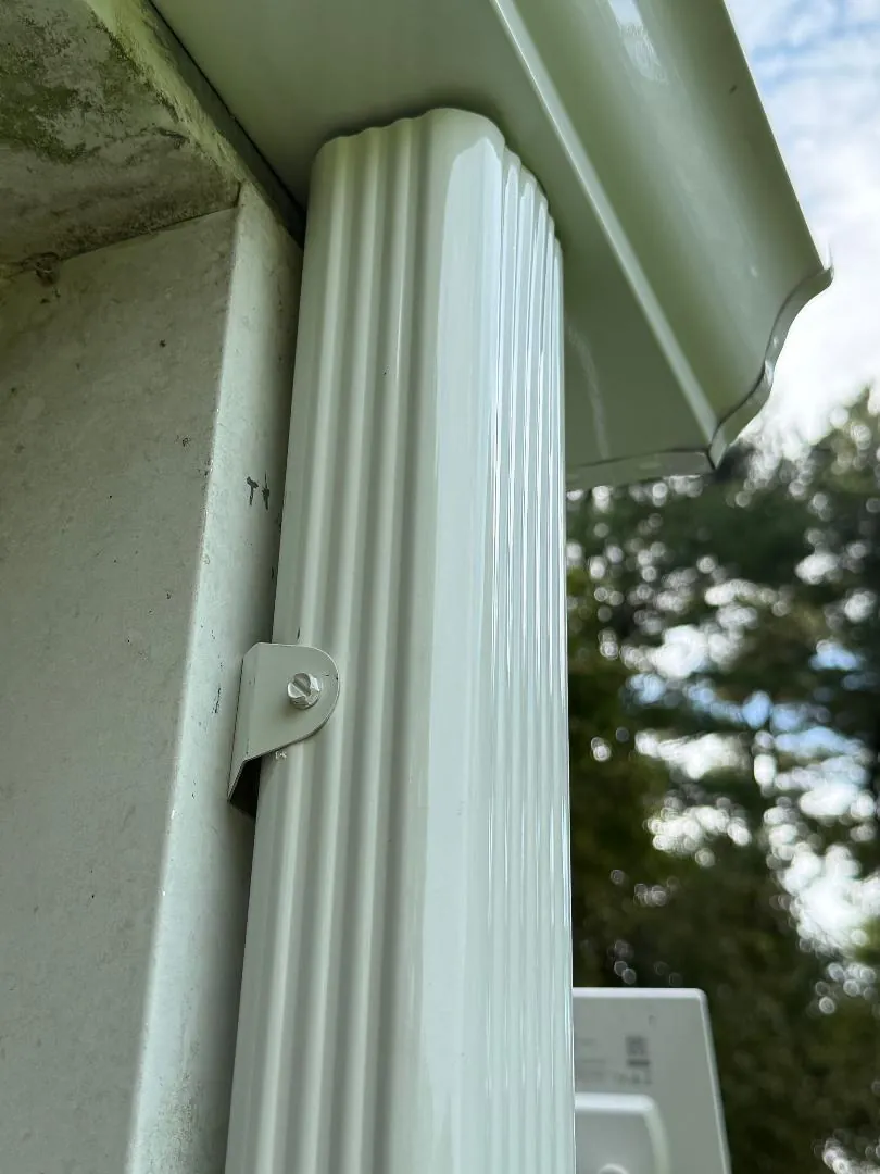 Close-up of a white corrugated downspout secured with a metal bracket below the gutter.