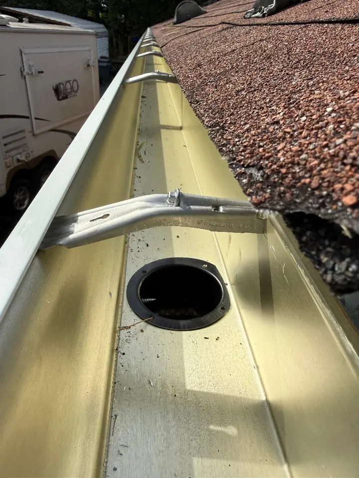 Interior of a light-colored rain gutter showing metal support hardware and the circular downspout outlet.
