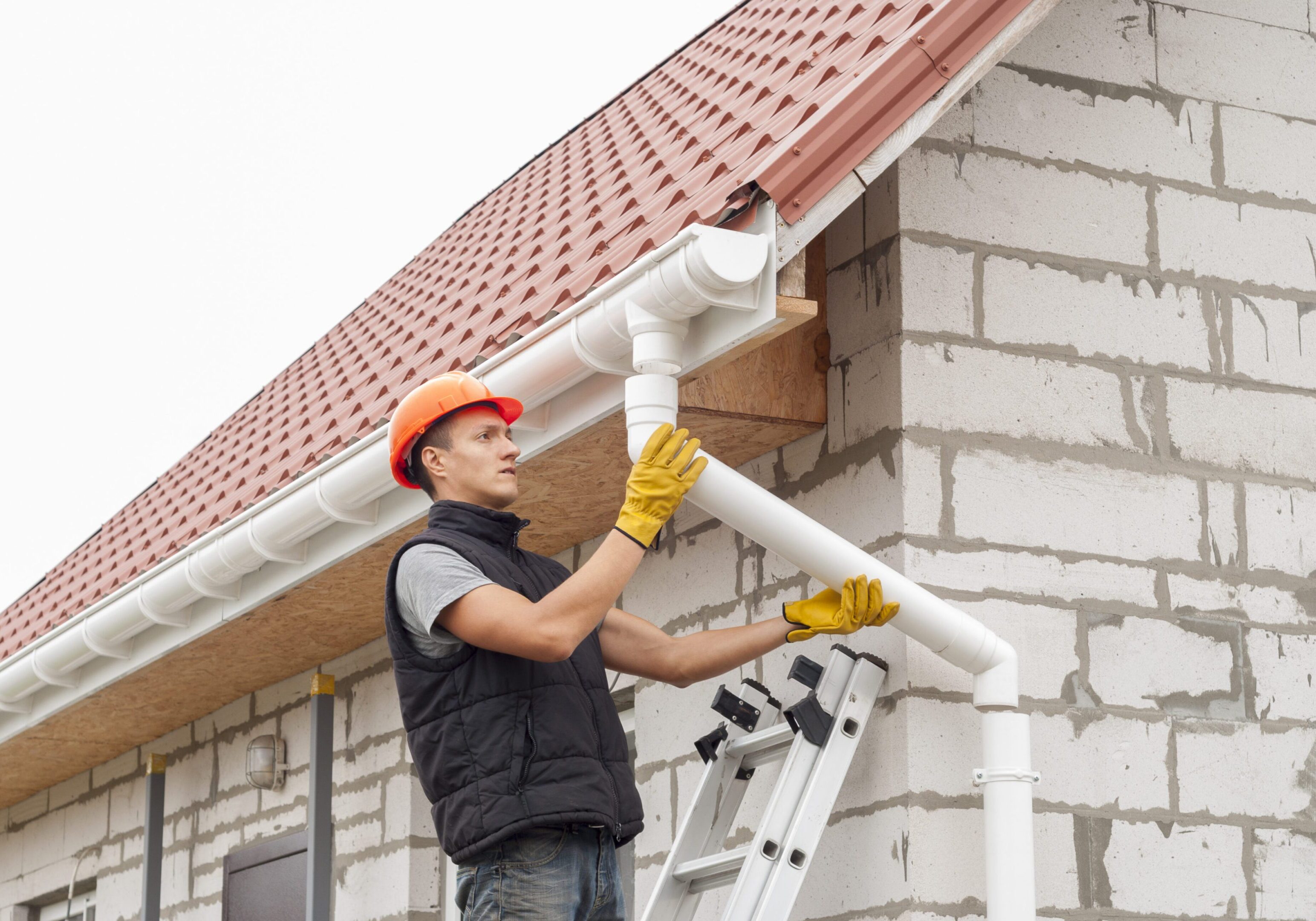 Worker installing gutters on a house roof.